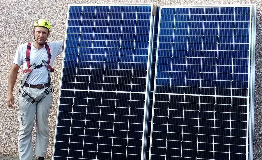 Tecnico S.O.S Luce con casco e imbracatura di sicurezza accanto a due moduli fotovoltaici
